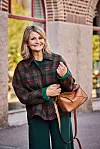 Margareta Hallin i gröna dressade byxor och tunn jacka med rutmönster i grönt och brunt. Hon har en brun väska över armen.