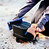 Person justerar en liten portabel grill som står på sandig mark.