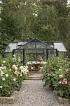Svart orangeri med dukat bord omgivet av höga blomrabatter och skog i bakgrunden.