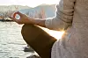 Närbild av person som mediterar vid en sjö i solnedgång med berg i bakgrunden.