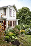 Tvåvånings trähus med frodig, färgstark trädgård på sluttande tomt.