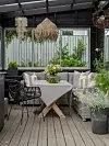 Inglasad uteplats med hörnsoffa, dukat bord, stolar och omgivande växter.