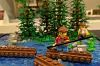 Lego-figur på brun flotte styr över blått vatten framför gröna Lego-träd.