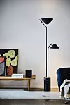 Svart golvlampa med två skärmar bredvid bänk med tavla i modernt vardagsrum.