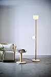 Golvlampa i trä med två glaskupor intill soffa och litet bord i ett ljust rum.