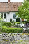 Uteplats med trädgårdsmöbler omgiven av klippta häckar framför ett äldre hus.