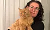 Kvinna med mörkt hår och glasögon håller en orange långhårig katt i famnen.