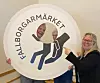 Tre personer håller upp en stor rund skylt med logotypen Fallborgarmärket inomhus.