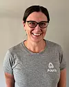 Karen Elise Di Bernardo, fysioterapeut. Hon ler mot kameran och har en grå t-shirt och glasögon.