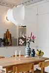 Ljust kök med träbord, blommor i vas, fruktskål och stor vit taklampa.