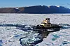 Isbrytare bryter en ränna genom havsis framför snötäckta berg