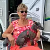 Äldre kvinna sitter i campingstol med hund i knät framför en parkerad husbil.