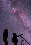 Silhuetter av två personer vid ett teleskop under en klar stjärnhimmel med Vintergatan.
