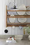 Tallriksställ i trä med gamla fat över bänkskiva med ägg och keramikskål i ljust kök.