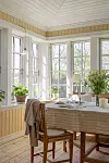 Ljus matsal med dukat bord, trästolar och stora spröjsade fönster mot grönska.