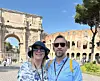 Två turister framför Colosseum och Konstantinbågen i Rom en solig dag.