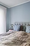 Soveværelse med blå væg, polstret sengegavl og sengetøj i neutrale farver