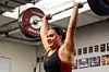 Kvinna lyfter en tung skivstång över huvudet i ett gym.