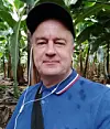 Man i blå pikétröja med hörlurar står bland bananplantor på en plantage.