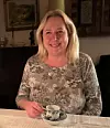 Leende person sitter vid dukat bord och håller en liten kaffekopp.