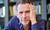 David Lagercrantz sitter lutad mot handen framför en bokhylla och ser in i kameran.