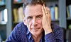 David Lagercrantz sitter lutad mot handen framför en bokhylla och ser in i kameran.
