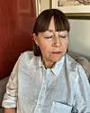 Kvinna i ljus skjorta sitter inomhus och tittar nedåt åt sidan Hon har fem akupunkturnålar i höger öra.