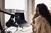 Person vid skrivbord med laptop och mikrofon-arm framför stort fönster.