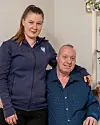 Stående och sittande person poserar tillsammans i ett vardagsrum