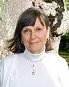 Kvinna i vit tröja står framför ett träd i en grön park.