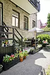 Grön innergård med trappa, blomlådor, utemöbler och parasoll intill tegelhus.