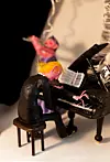 Närbild av små färgglada figurer som spelar piano och flöjt vid en svart flygel.