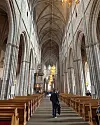 Interiör av gotisk katedral med höga valv, träbänkar och en person som går i mittgången.