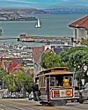 Kabelspårvagn färdas nedför backe med utsikt över hamn och segelbåt i San Francisco