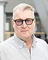 Äldre man med glasögon ser in i kameran i en ljus inomhusmiljö.