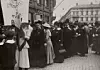 Svartvit bild av kvinnor i hattar i ett demonstrationståg med banderoll om rösträtt.