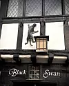 Fasad på Black Swan med svart kattdekor och vägglykta ovan entrén.