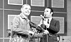 Folkmusiker med fiol och programledare vid mikrofon i tv-studio.