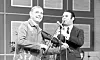 Folkmusiker med fiol och programledare vid mikrofon i tv-studio.