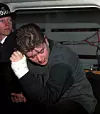 Person med bandagerad arm böjer sig ner bredvid polis i ett fordon.