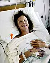 Leende patient med dropp ligger nerbäddad i vit sjukhussäng på vårdavdelning.