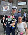 Student med mössa och plakat firas utanför skola tillsammans med leende anhörig.