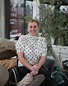 Kvinna i prickig blus sitter i rullstol i ljust rum med växter