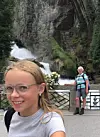Äldre kvinna och flicka poserar framför ett stort vattenfall i bergig miljö.