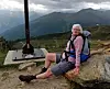 Äldre kvinna med ryggsäck vilar på bergshäll vid vandringsled i Alperna.