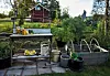 Trädgårdsbord med skörd och odlingsbäddar framför ett rött hus på landet.