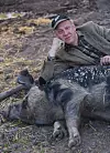 Man i keps och kavaj ligger i en hage bredvid ett vilande linderödssvin.