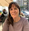 Kvinna sitter vid ett cafébord utomhus i stadsmiljö en solig dag.