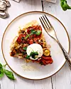Bit grönsakspaj med burrata och basilika på vit tallrik med gaffel.