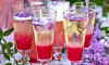 Tvåfärgade sommardrinkar i höga glas med lila blomblad på ett dukat bord utomhus
